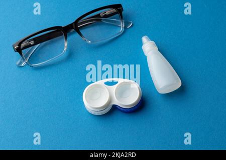 Composizione di occhiali con custodia per lenti a contatto e collirio e su sfondo blu con spazio copia Foto Stock