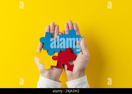 Composizione delle mani che tengono pezzi di puzzle jigsaw su sfondo giallo con spazio di copia Foto Stock