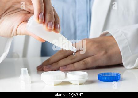 Sezione centrale di una dottoressa caucasica che riempie il contenitore della lente a contatto con una soluzione di lente Foto Stock