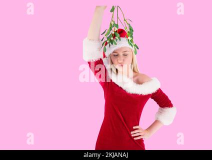 Donna caucasica che indossa il costume di santa tenendo una vischio contro spazio copia su sfondo rosa Foto Stock