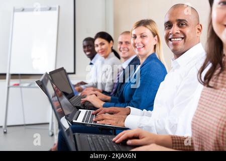 Vista laterale dell'allegro uomo d'affari ispanico con computer portatile durante il seminario Foto Stock