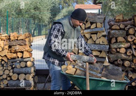 Immagine di un uomo che carica pezzi di legno su una carriola per accendere il fuoco nel camino. Riscaldamento in previsione dell'inverno Foto Stock