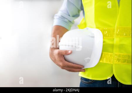 L'ingegnere tiene in mano l'elmetto con un giubbotto giallo e si trova pronto per la sicurezza sul lavoro in loco. Foto Stock