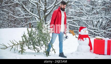 Santa uomo in posa con ascia e albero di Natale. L'uomo sta andando tagliare un albero di Natale. Un bel legname con barba porta un albero di Natale. Foto Stock