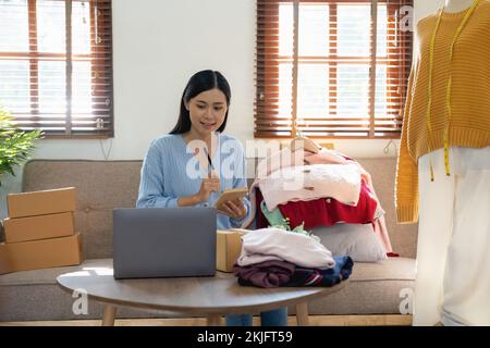 Bella donna rivedere i vestiti e la telecamera parlante live registrazione video sul social network a casa, vendita online di abiti sui social media Foto Stock