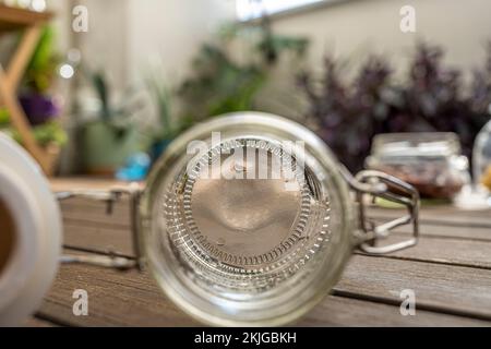 Vaso di vetro vuoto e trasparente con sigillo sottovuoto su tavole di legno di acacia e piante sullo sfondo Foto Stock