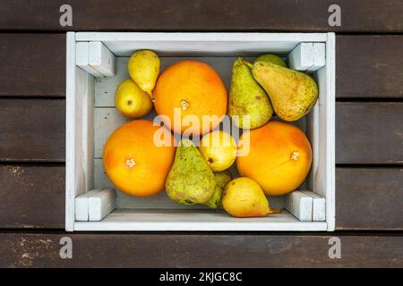 Una scatola di legno piena di agrumi maturi e pere assortite Foto Stock