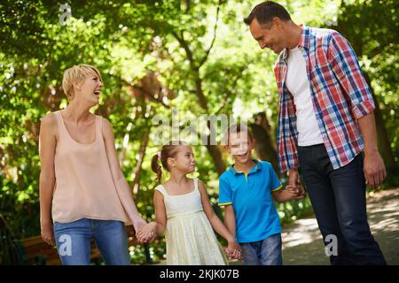 Una famiglia felice è un paradiso precedente. Un breve scatto di una felice famiglia a piedi attraverso un parco in una giornata di sole. Foto Stock