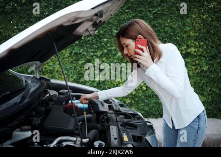 Donna che utilizza il telefono cellulare per richiedere assistenza dopo un guasto dell'auto sulla strada. Foto Stock