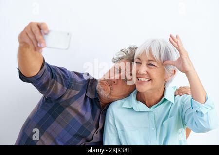 Crescere è facoltativo. una coppia anziana affettuosa che gioca intorno mentre scatta le foto di se stessi con un telefono cellulare. Foto Stock