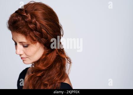 Capelli belli per una principessa. Studio shot di una giovane donna con bei capelli rossi che si posano su uno sfondo grigio. Foto Stock