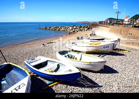 Piccole barche ormeggiate sulla spiaggia con vista verso la passeggiata e le scogliere, Sidmouth, Devon, UK, Europa. Foto Stock