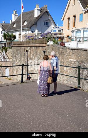 Vista delle case di paglia che si affacciano sulla spiaggia con una coppia in piedi in primo piano, Sidmouth, Devon, Regno Unito. Foto Stock