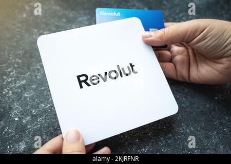 Carta Revolut Bank con la busta bianca in mano. Nuova scheda Revolut blu ridisegnata su fondo in cemento. Cracovia, Polonia - 11 novembre 2022. Foto Stock