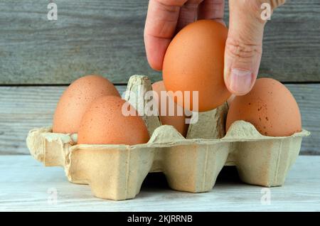 Persona che prende uovo di pollo da scatola, sfondo di legno Foto Stock