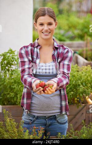 Godendo dei frutti del suo lavoro. una giovane donna felice che tiene una manciata di fragole appena raccolte. Foto Stock