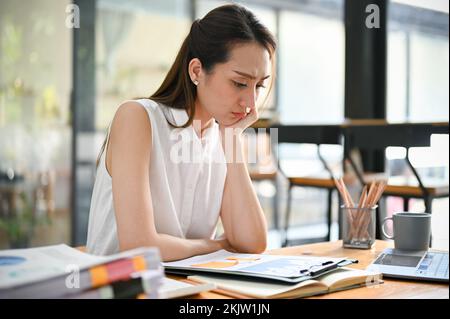 Ha sottolineato la donna d'affari asiatica millennial o il manager femminile concentrandosi a leggere ed esaminare il rapporto finanziario alla sua scrivania. Foto Stock