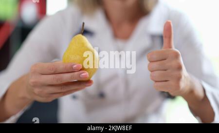 Medico che tiene in mano la pera gialla matura e che mostra il segno del pollice in su Foto Stock