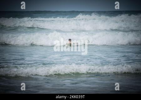 Un surfista cavalca le onde nei mari accidentati al largo della costa occidentale francese vicino a Mimizan, Francia Foto Stock