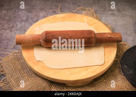 Un primo piano di un impasto teso con un matterello su un piatto di legno Foto Stock