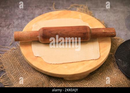 Un primo piano di un impasto teso con un matterello su un piatto di legno Foto Stock