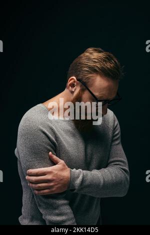 Elegante uomo sconvolto in occhiali a contatto braccio isolato su nero, immagine stock Foto Stock