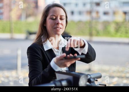 Donna d'affari nel suo 40s noleggio e-scooter con app per smartphone in città Foto Stock