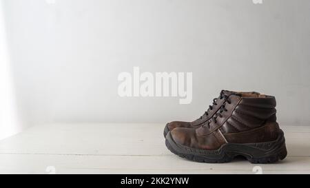 vista ravvicinata di un paio di scarpe di sicurezza rustiche usate in cima a un pavimento in legno bianco e uno sfondo bianco Foto Stock