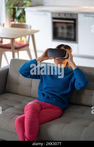 La giovane donna indossa occhiali VR ed esplora giochi interessanti con una grafica straordinaria a casa Foto Stock