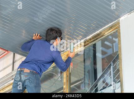 Lavoratore installare soffitto in lamiera di metallo in edificio. Utilizzare un cacciavite per fissarlo. Foto Stock