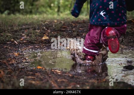 Un primo piano di un bambino che fa un passo nella pozza in una giornata piovosa Foto Stock