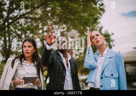 Bell'uomo d'affari che mostra qualcosa ai suoi colleghi mentre si trova al parco Foto Stock