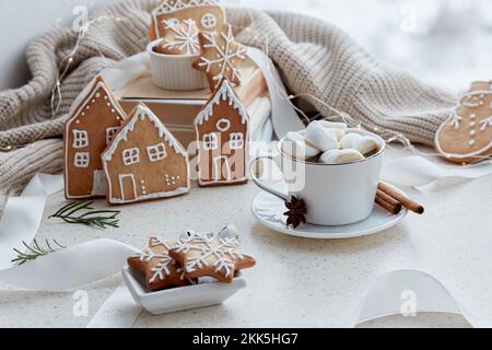 Cioccolata calda alle marshmallow con biscotti fatti in casa allo zenzero a forma di graziose case e fiocchi di neve. Estetica sfondo di Natale femminile. Foto Stock