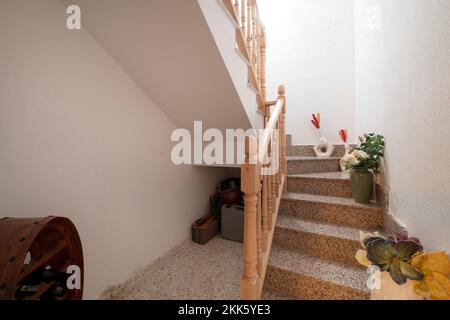 Scala interna di casa indipendente con pavimenti in granito rosa, ringhiera in legno grezzo e oggetti decorativi sulla scala Foto Stock