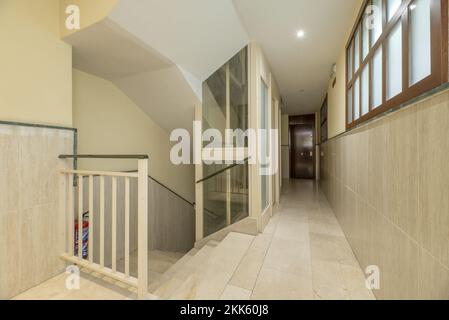 Atterraggio di un edificio residenziale con una scala con pavimenti in marmo crema, ringhiere in metallo bianco e ascensore in metallo e vetro Foto Stock