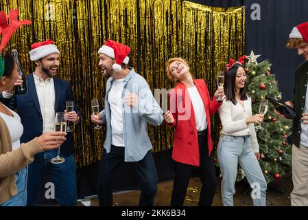 Uomini d'affari multietnici con champagne ballare durante la celebrazione di Natale in ufficio Foto Stock