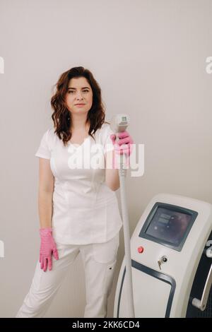 Ritratto del maestro della rimozione dei peli del laser. Una donna in un cappotto bianco tiene un dispositivo di rimozione dei capelli del laser nelle sue mani Foto Stock