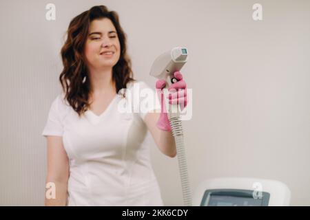 Ritratto del maestro della rimozione dei peli del laser. Una donna in un cappotto bianco tiene un dispositivo di rimozione dei capelli del laser nelle sue mani Foto Stock