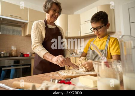 Vecchia donna che prepara la pasta per la cottura con il nipote Foto Stock