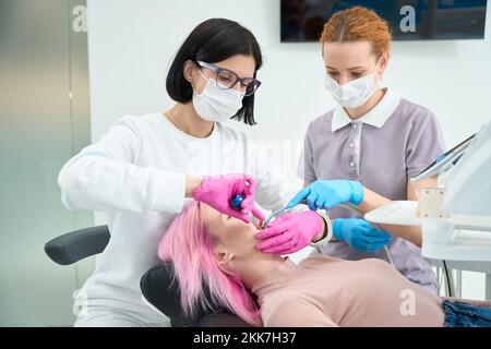 Assistente aiuta il dentista donna nell'installazione del sistema di rinforzi per il paziente giovane Foto Stock