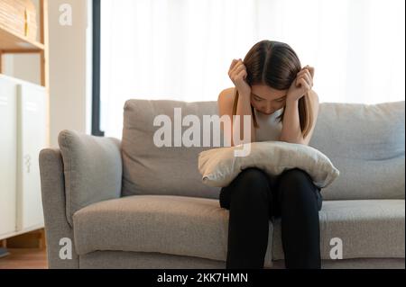 Una giovane donna asiatica che si sente depressa e infelice seduto su un divano a casa Foto Stock
