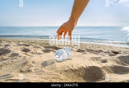 Una mano si abbassa per prendere una bottiglia d'acqua scartata Foto Stock