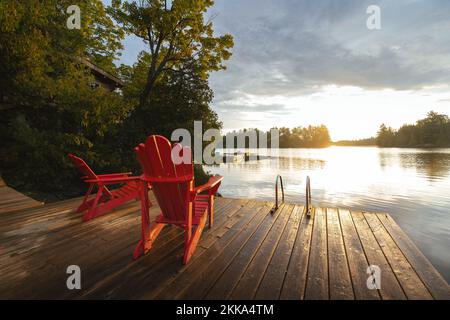 Due sedie rosse si siedono di fronte all'alba su un molo Foto Stock