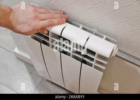 Radiatore di riscaldamento domestico bianco a contatto con la mano maschile. Moderna tecnologia di riscaldamento casa. Foto con messa a fuoco selettiva per primo piano. Foto Stock