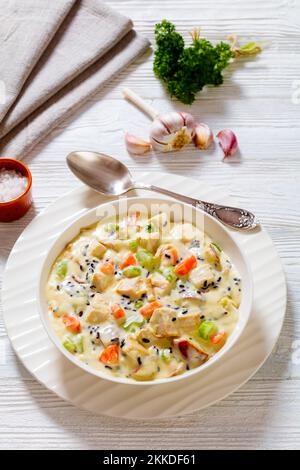 Zuppa cremosa di riso selvatico tacchino con patate rosse. carota, sedano, spezie ed erbe in ciotola bianca su tavolo di legno, vista verticale Foto Stock