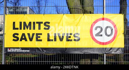 Il banner del limite di velocità dice "Limits Save Lives" (limiti salvare vite) con un suggerimento di 20 miglia all'ora sul recinto di una scuola a Manchester, Regno Unito Foto Stock