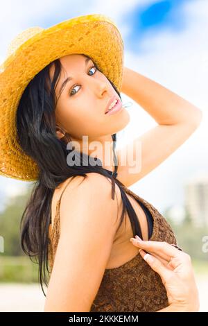 Bella donna bikini che indossa cappello da sole con incantato e felice Espressione di una bellezza senza tempo di fronte a un'estate nuvolosa Cielo Foto Stock