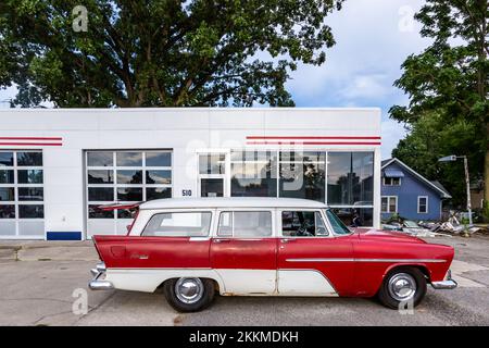 Un antico carro della stazione Suburban 1956 di Plymouth, rosso e bianco, parcheggiato di fronte ad una stazione di servizio ad Auburn, Indiana, USA. Foto Stock