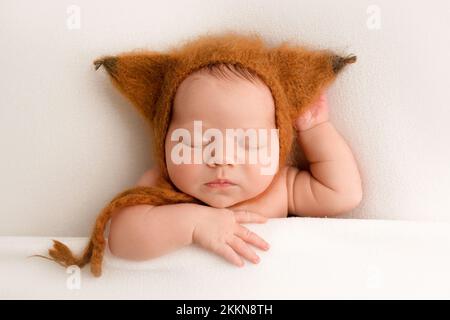 Una bambina appena nata nei primi giorni di vita in una cuffia marrone con orecchie carine. Macro studio ritratto di un bambino su sfondo bianco. Vista dall'alto. Foto Stock