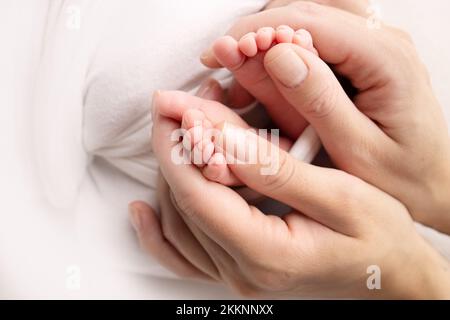 La madre sta facendo il massaggio sul suo piede del bambino. I piedi del bambino nelle mani della madre su un bianco. Foto Stock